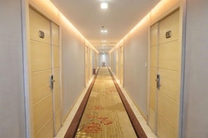 A hotel hallway with doors on both sides, a carpet with a floral pattern, and overhead lighting. - Meinaya Hotel (Kunming)