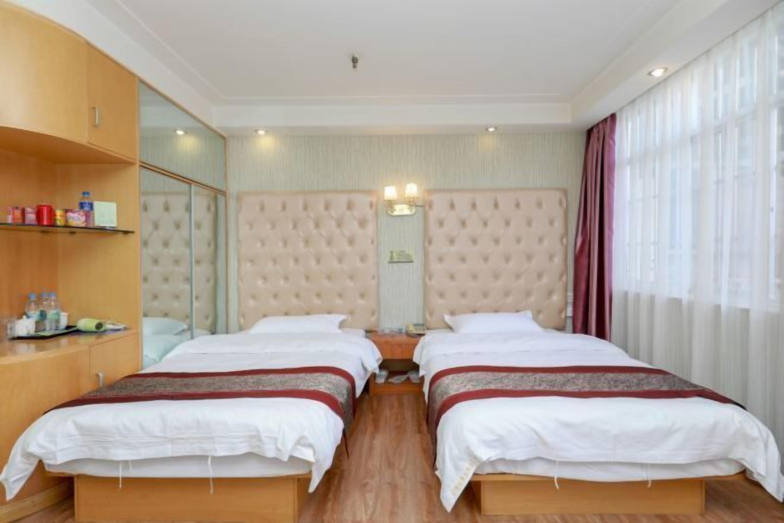 A hotel room with two beds, a wooden wardrobe, a mirror, and a large window with curtains.