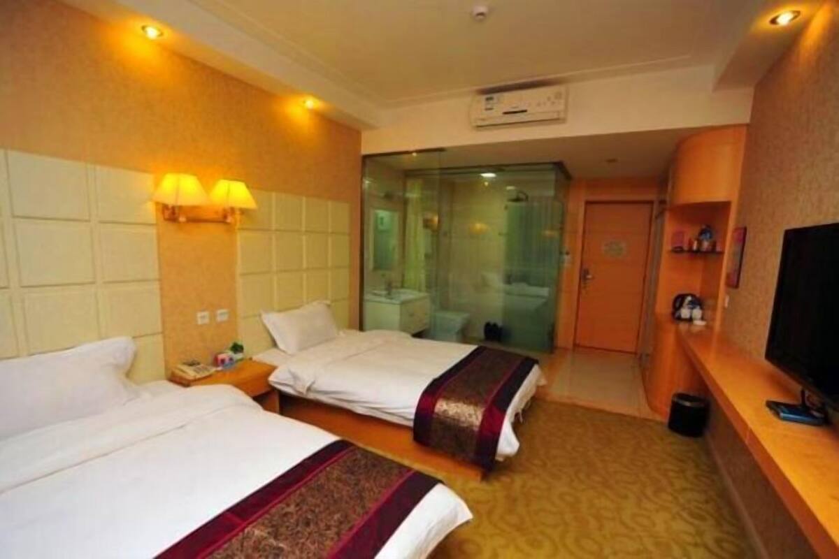 A hotel room with two beds, a TV, a mirror, and a bathroom visible through a glass door.