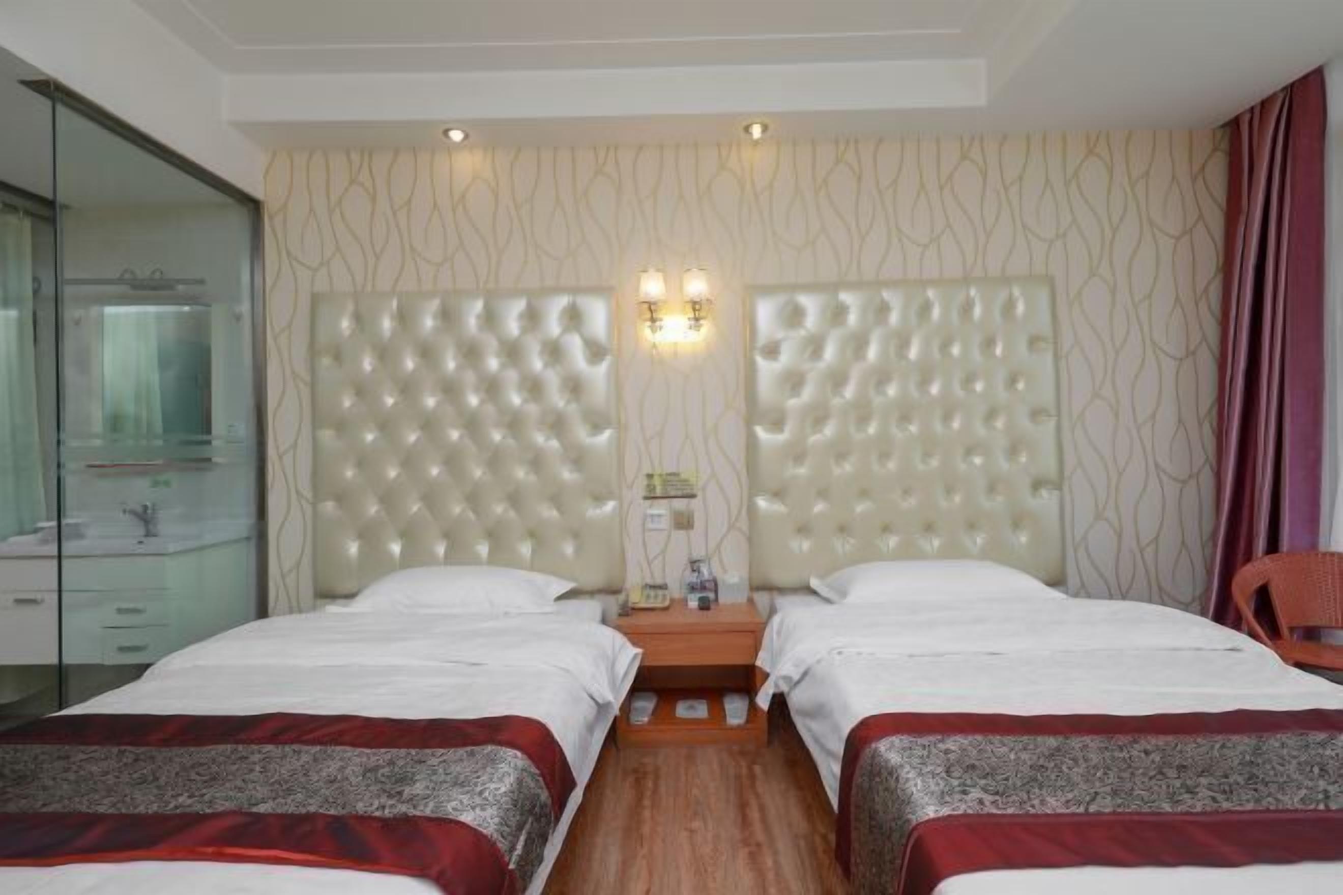 Habitación de hotel con dos camas, piso de madera, separador de vidrio y lámpara fijada a la pared.