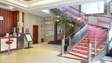 Een hotel lobby met een receptiebalie, een trap met roze leuningen en een grote plant.