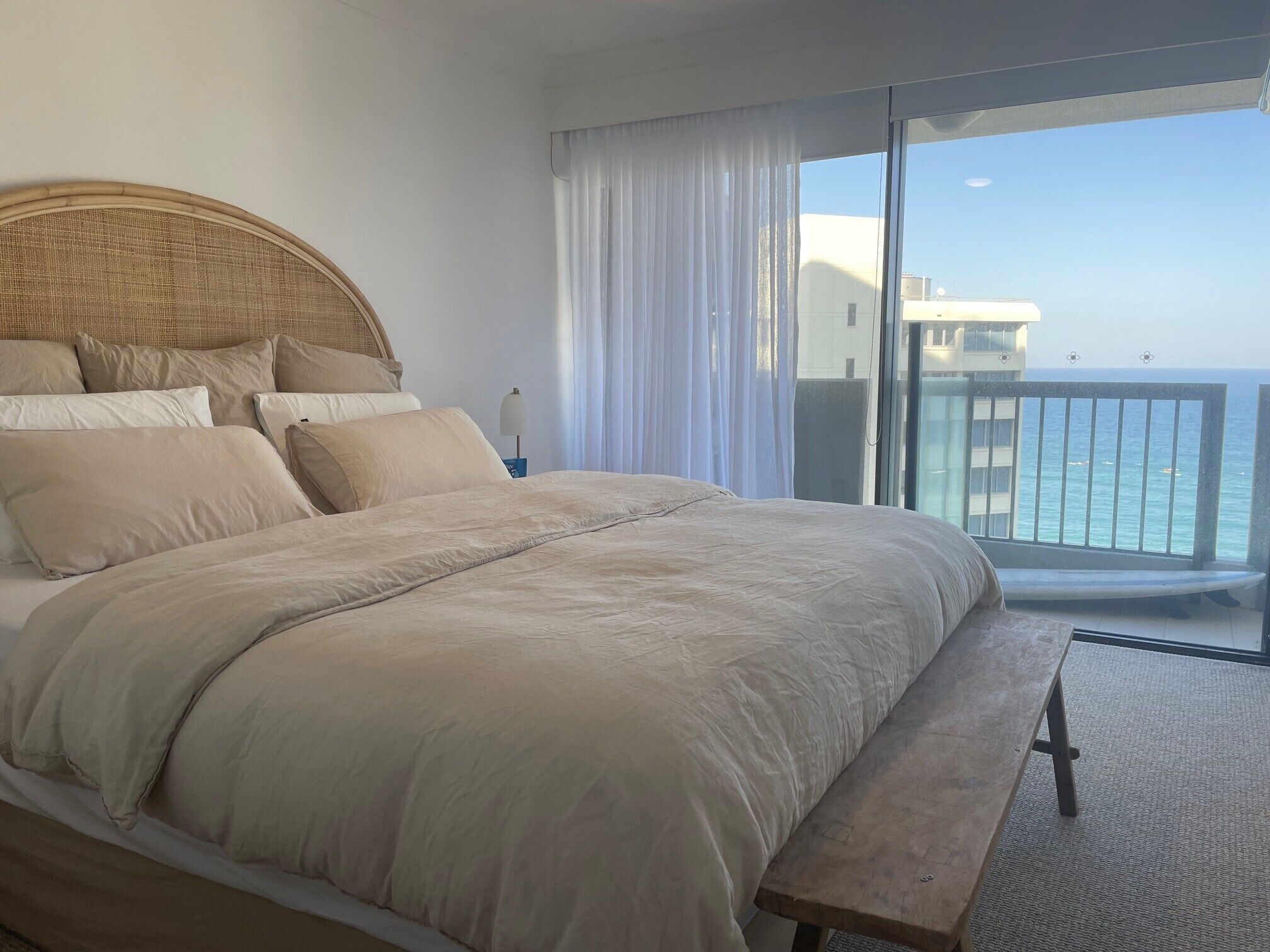 Een slaapkamer met een groot bed, een houten bankje en uitzicht op de oceaan vanuit een balkon.