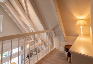 Ein Zimmer mit hohen Decken, freiliegenden Holzbalken, einem weißen Geländer und einem Tisch mit Lampe.