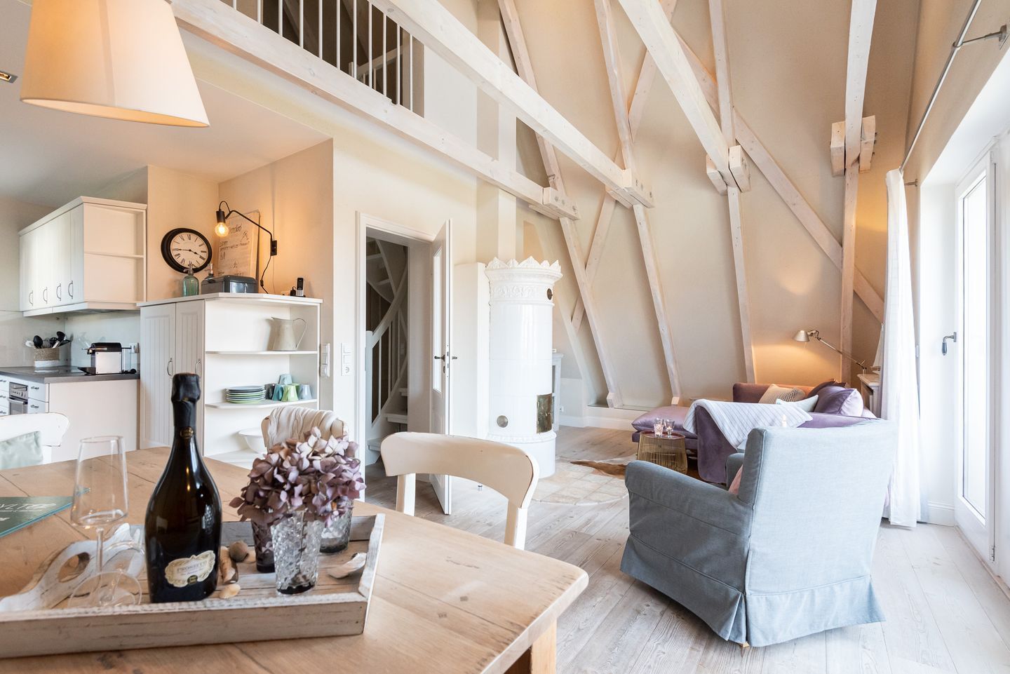 A spacious loft with a high ceiling, exposed wooden beams, a dining area with a table set for two, and a cozy seating area with a sofa and armchairs.