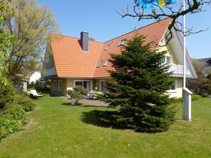 Ein zweistöckiges Haus mit rotem Ziegeldach, einem Balkon und einem gepflegten Rasen.