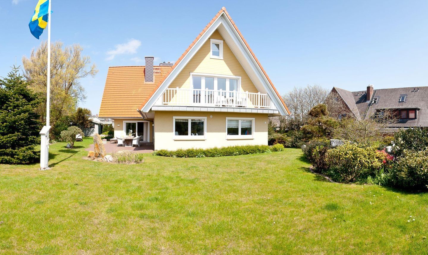 A two-story house with a sloped roof, a balcony, and a well-maintained lawn.