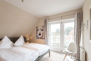 Ein Schlafzimmer mit Bett, einem Sessel, einem Nachttisch, einem Gemälde und Blick durch eine Glastür.