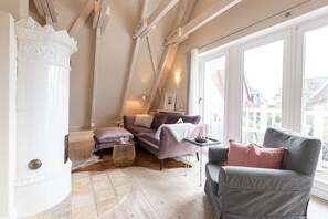 Ein gemütliches Schlafzimmer im Loft-Stil mit schrägem Dach, einem großen Fenster, einem violetten Sofa, einem grauen Sessel und einem kleinen Beistelltisch.