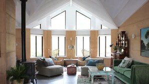 Ein geräumiges Wohnzimmer mit hoher Decke, großen Fenstern, einem Kamin und einem grünen Sofa.