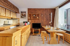 A wooden kitchen with a TV, wooden cabinets, and a dining area with a table and chairs. - Résidence Devouassoux F ski in/ski out, Argentière (Chamonix), France (Argentière (Chamonix))