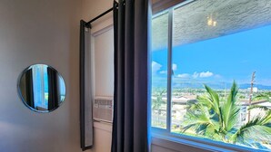 A room with a large window, a round mirror, and a ceiling fan. - Unit 18 Waena Inn - Maui Private Suite (Wailuku)