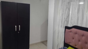 Un dormitorio con un armario negro, una cama con cabecero rosa y una cortina blanca.