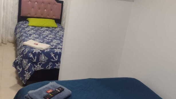 Un dormitorio con una cama, televisor montado en la pared y una ventana con cortinas.