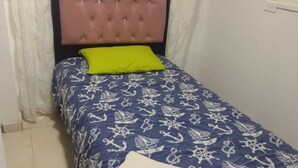 Una cama individual con cabecera rosa, colcha con motivos náuticos en azul y blanco, y almohada verde.