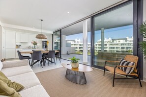 A modern apartment with a dining area, a sofa, a coffee table, and a view of the city through large windows. - Deco | Pool - Terrace - Parking (Fuengirola)