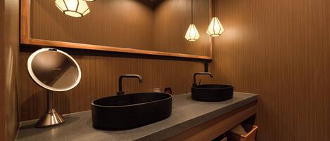 A bathroom with a wooden vanity, two black sinks, a round mirror, and pendant lights.