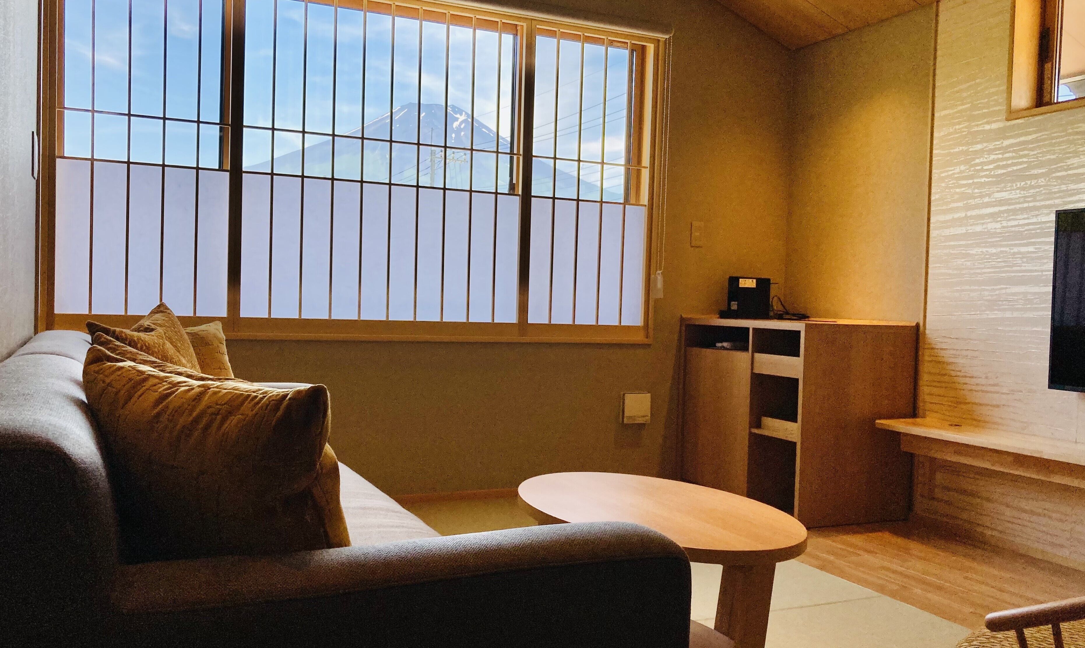 Ein Zimmer mit einer Couch, einem kleinen Tisch, einem an der Wand befestigten Fernseher und einem Fenster mit Bergblick.
