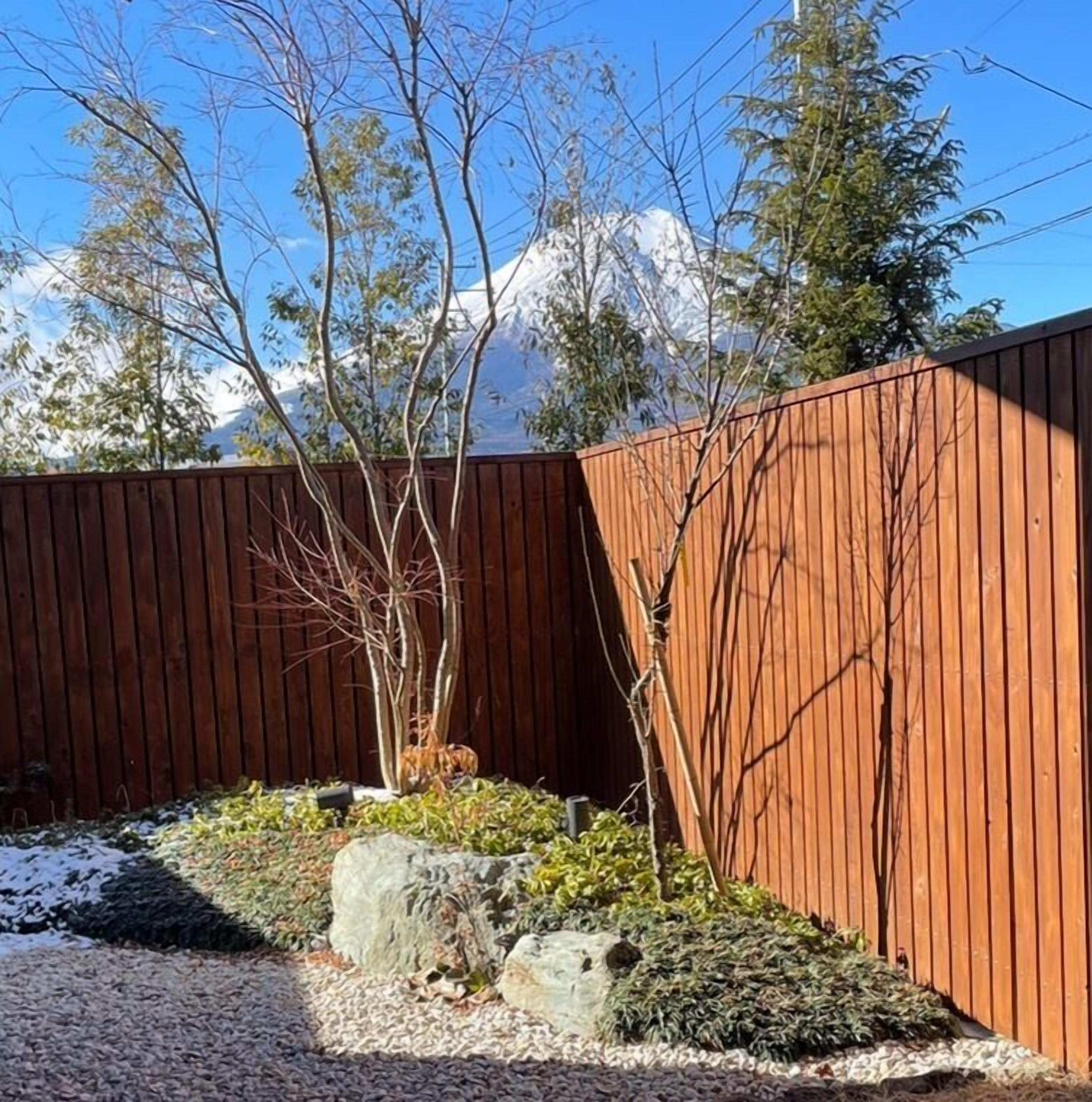 A wooden fence with a small tree and rocks in a garden area.