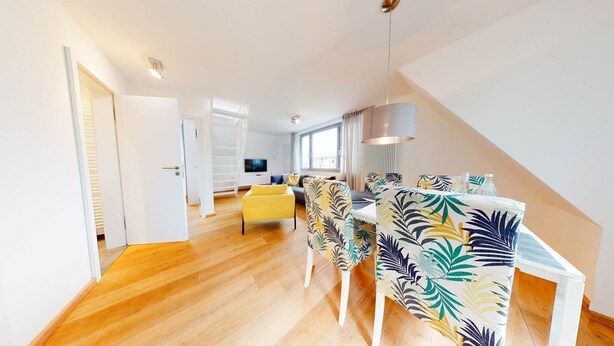 Un salon moderne avec un plancher en bois, un canapé, une table à manger avec des chaises à motifs et un téléviseur en arrière-plan.