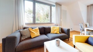 Un salon moderne avec un canapé gris, des coussins aux motifs jaunes et noirs, une table basse blanche et un fauteuil jaune.