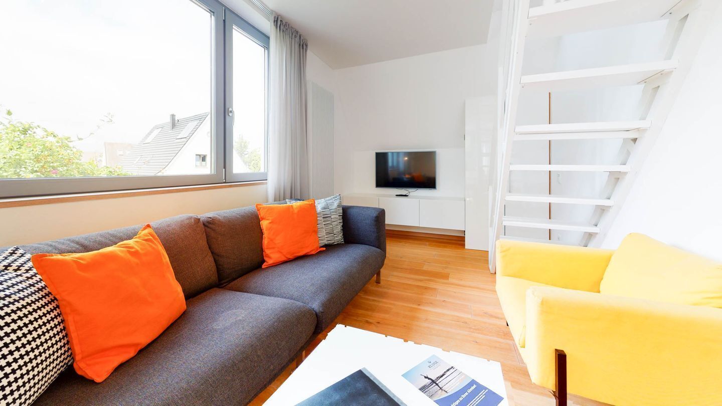 Een moderne woonkamer met een grijze bank, een gele fauteuil en een flatscreen televisie.