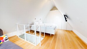 A modern, white-themed bedroom with a loft bed, wooden flooring, and a white wardrobe.