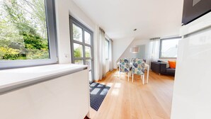 A modern, well-lit room with large windows, a dining area with patterned tablecloths, and a grey sofa.