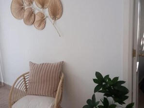 A wicker chair with a striped cushion against a white wall, a potted plant, and a wall decoration of circular shapes.