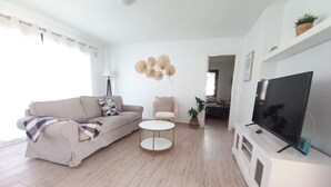 A modern living room with a sofa, a round coffee table, a TV on a stand, and a wall-mounted plant.