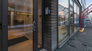 A building entrance with a glass door, a number '103' on the door, and a small outdoor seating area visible through the glass. - Central & Modern Apartment Reykjavik with balcony 204 (Reykjavík)