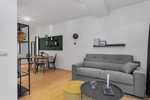 A modern living room with a grey sofa, a round coffee table, and a dining area with a wooden table and chairs.