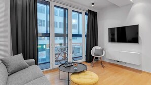 A modern living room with a sofa, ottoman, and a flat-screen TV mounted on the wall. - Central & Modern Apartment Reykjavik with balcony 204 (Reykjavík)
