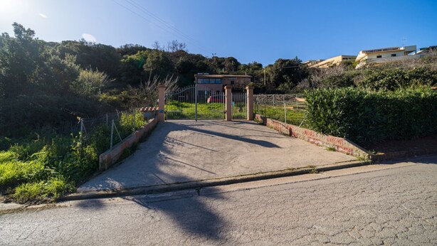 Un pas marcat que condueix a una propietat amb una zona enclavant, envoltada de vegetació i turons.