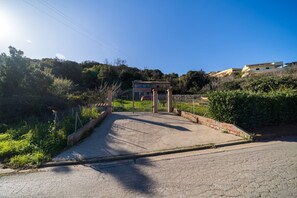 A paved entrance to a property with a gated area, surrounded by greenery and hills.