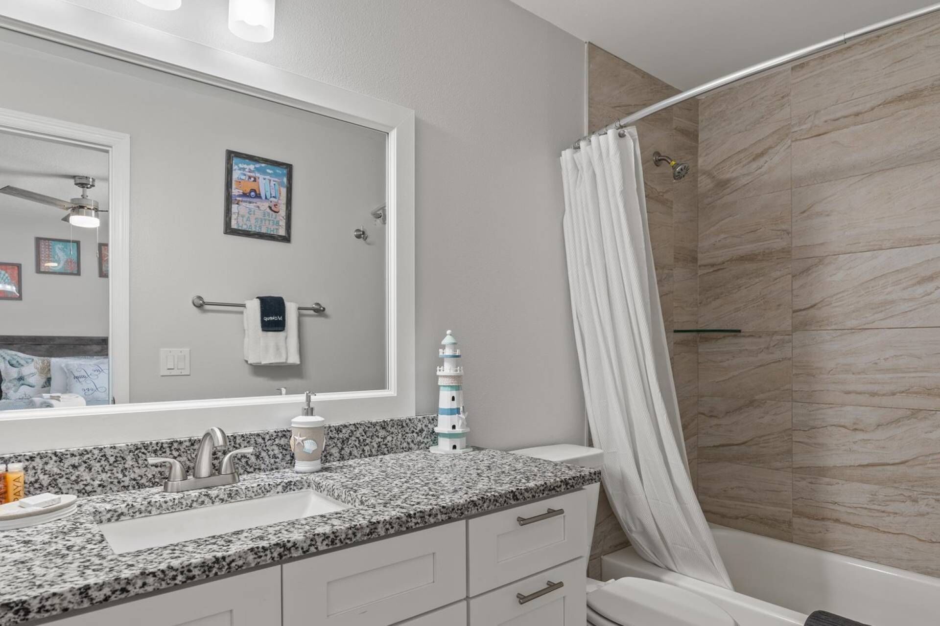 A bathroom with a granite countertop sink, a white toilet, and a shower with a curtain.