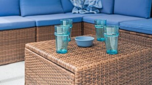 Un sofá de mimbre con cojines azules y una mesa de centro tejida con cristalería azul y un cuenco.