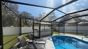 Un espacio exterior techado con piscina, sillas y vistas al jardín.