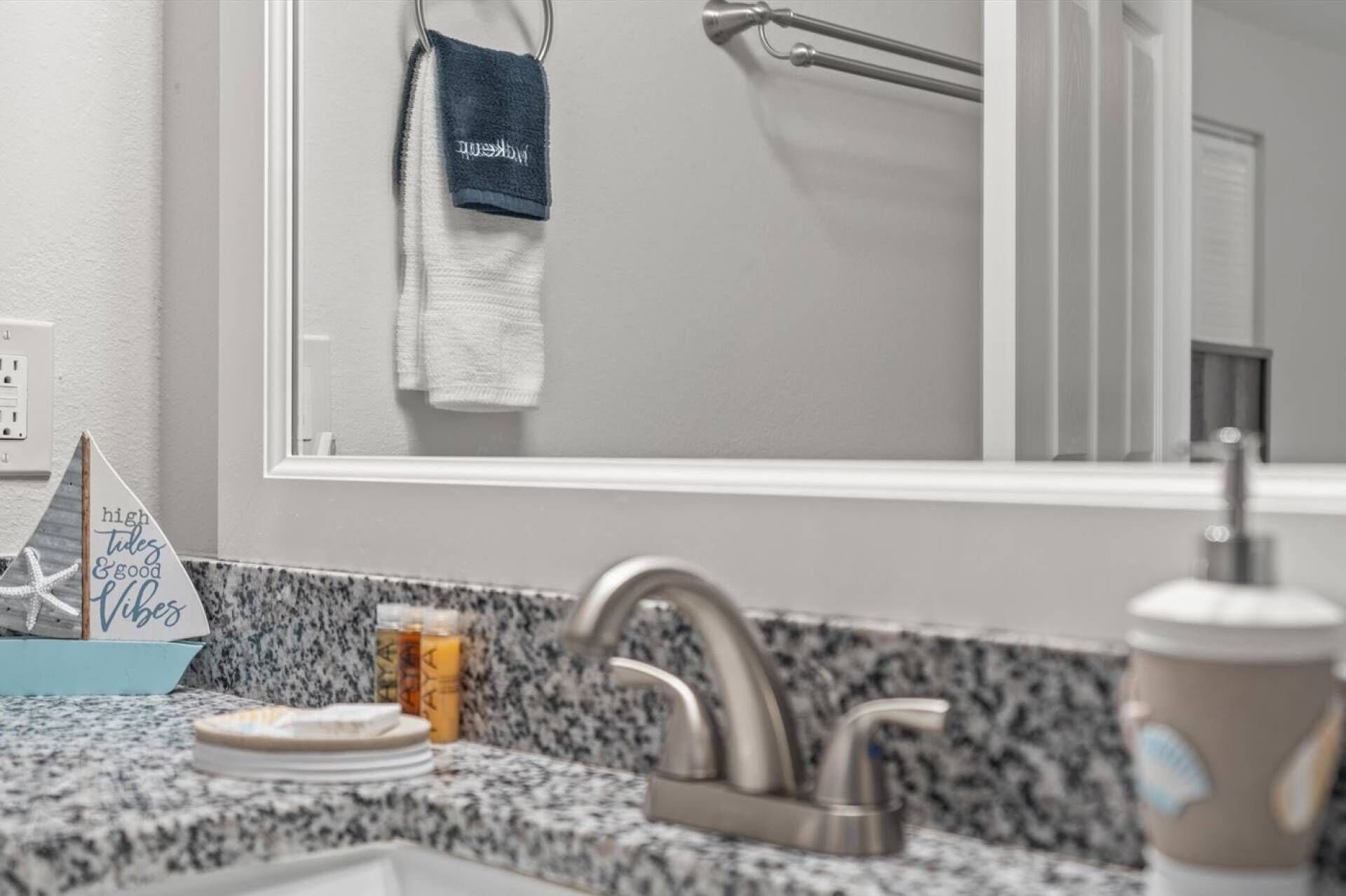 A bathroom with a granite countertop, a sink with a modern faucet, a towel rack with a blue towel, and a sign that reads "high tides & good vibes".