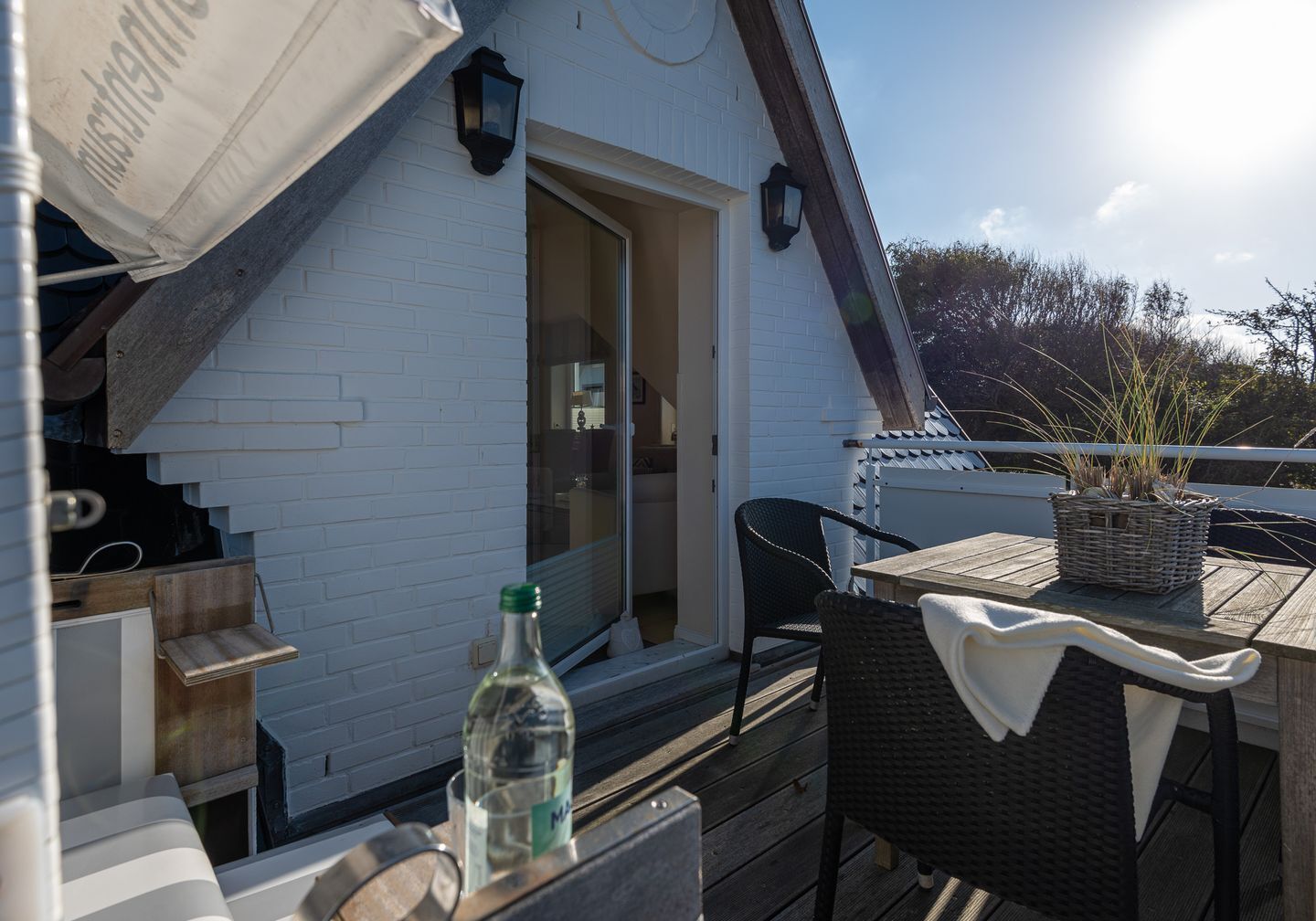 A wooden deck with a table and chairs, a bottle of water, and a basket of plants.