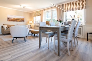 Un comedor con mesa y sillas de madera, un sofá y una ventana con cortinas.