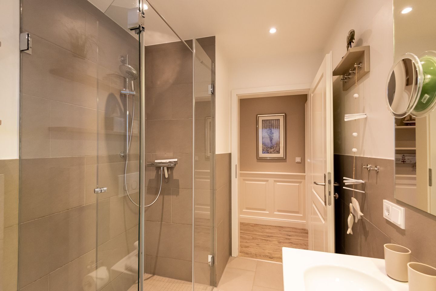 A modern bathroom with a glass-enclosed shower, a vanity with a mirror, and a wooden floor.