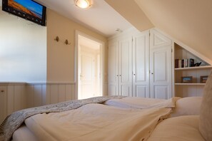 Un dormitorio con cama, televisor montado en la pared y estantería.