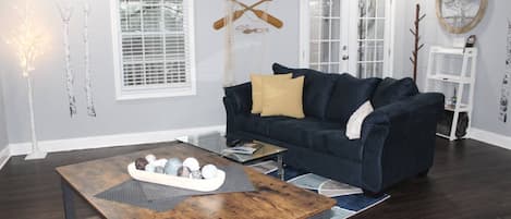 A living room with a dark blue sofa, a wooden coffee table, and a glass door with a sign above it.