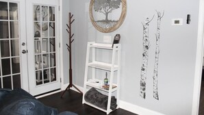 Ein Zimmer mit einer weißen Tür, einem Kleiderhaken, einem weißen Regal mit Gegenständen und einer Wand mit Baumkonturen.
