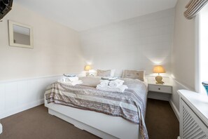 A hotel room with a bed, two bedside tables, a nightstand, a mirror, and a window with curtains.