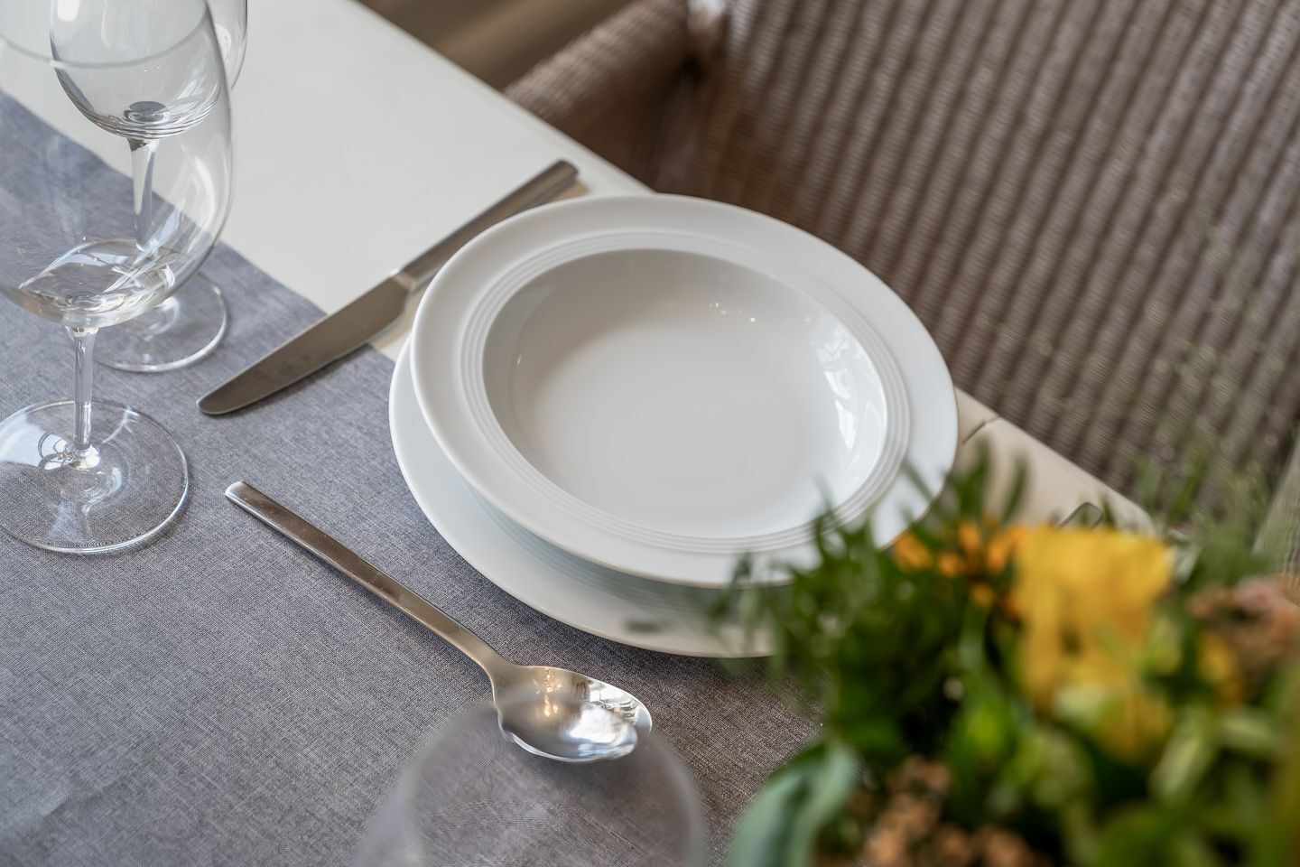 A table set with white plates, a spoon, and two wine glasses.