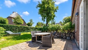 Eine Terrasse mit Tisch und Stühlen, einer Liege und einer Steinmauer.