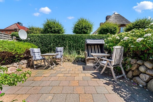 An outdoor patio with a table and four chairs, surrounded by a stone wall and greenery.