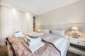 A hotel room with a large bed, a bedside table with a lamp, a wardrobe, and a small shelf. - Haus Borelör Whg. 1 EG - EG im Haus Börelör, 3-zimmerwohnung auf ca. 80 m² im EG für bis zu 4 (Sylt)
