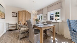 A dining area with wicker chairs, a wooden table, and a chandelier.